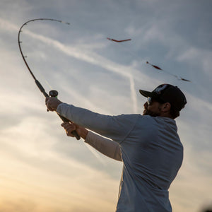 Angler casting an Ugly Stik fishing rod at sunset with the rod deeply bent.