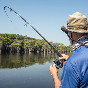 Angler fishing with an Ugly Stik spinning rod bent under load on a calm freshwater lake.