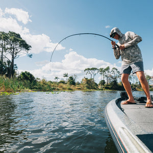 Bass angler fighting a fish from a boat with an Ugly Stik rod fully loaded.