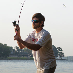 Angler casting an Ugly Stik spinning rod from shore at sunrise.