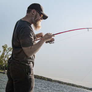 Angler fighting a fish with a red Ugly Stik spinning rod on a sunny day.