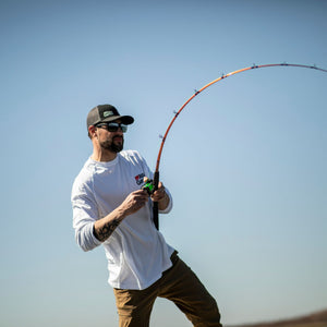 Angler fighting a fish with an Ugly Stik casting rod under clear blue skies.