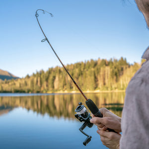 Ugly Stik Camo Dock Runner in a man's hand with a lake and trees blurred in the background. 