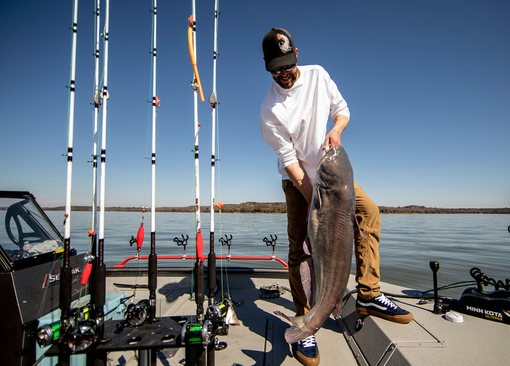 Man holding a large catfish on a dock with fishing rods in the background