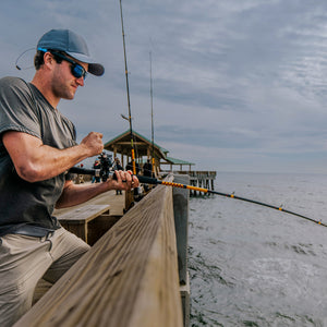 Man fishing off a pier with a Bigwater bent rod over water. He is wearing a green t-shirt, blue hat and sunglasses. 