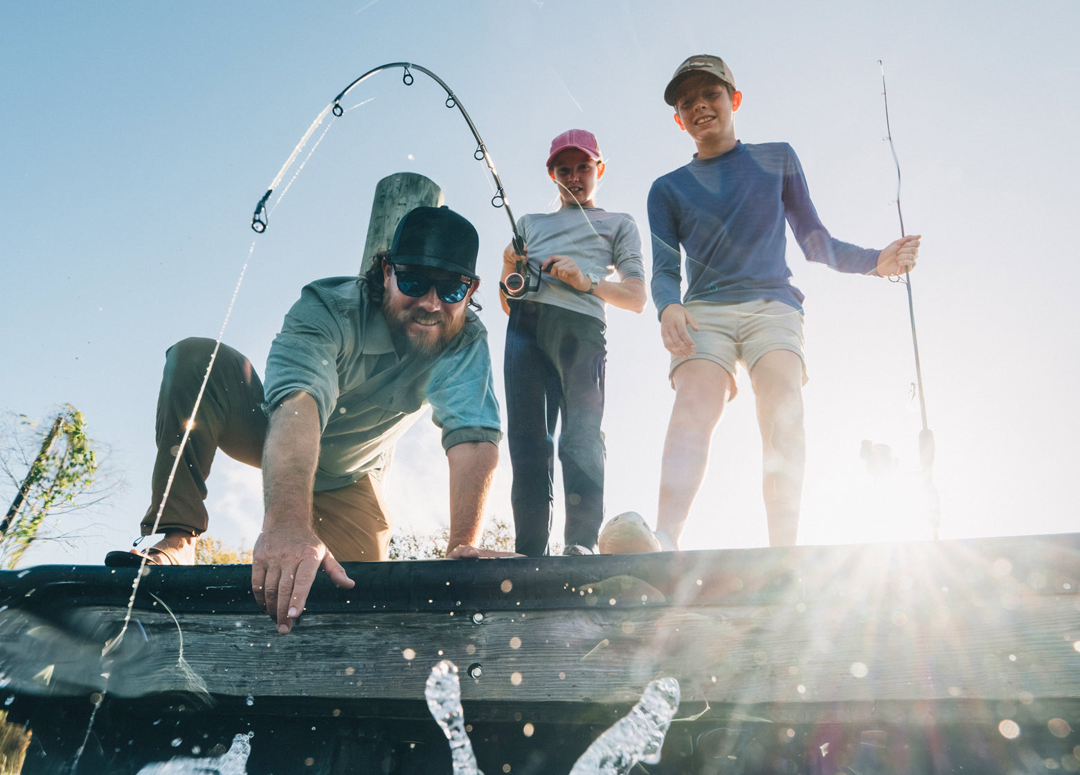 Three people fishing from a truck bed on a sunny day.