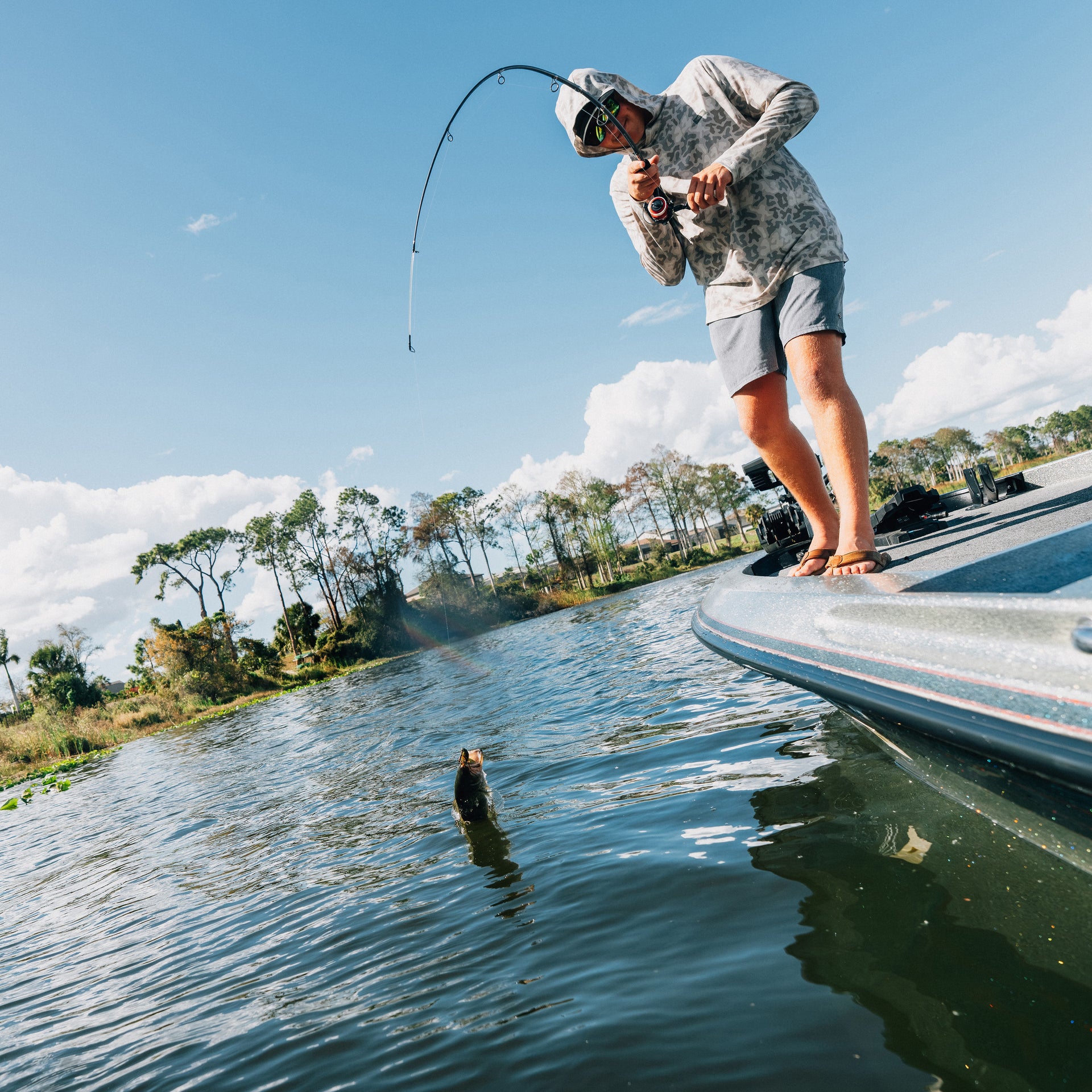 Person fishing from a boat on a calm lake with trees and sky in the background