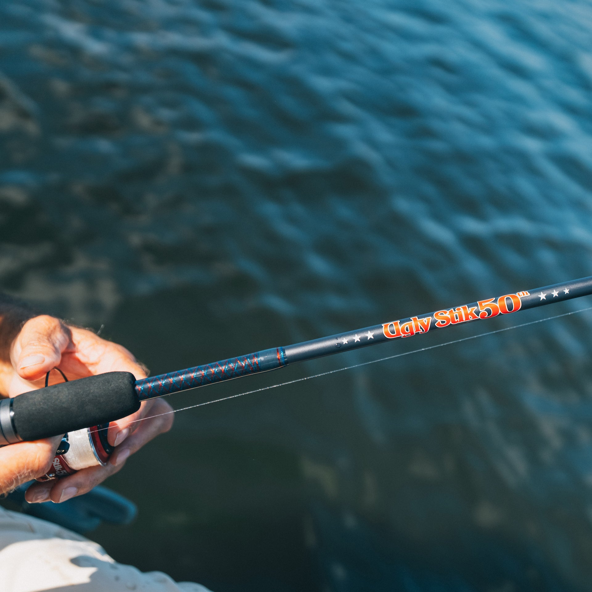 Fishing rod with 'Ugly Stik 50th' branding held by a person over water