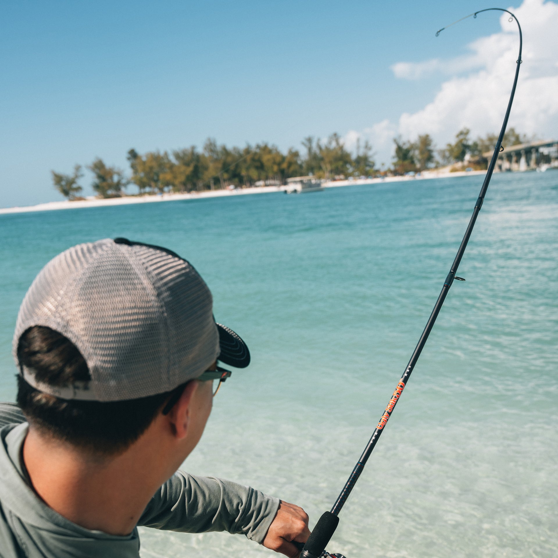 Man fishing at the ocean with an Ugly Stik 50th Anniversary combo bent over the water. He is wearing a hat and sunglasses facing the water. 