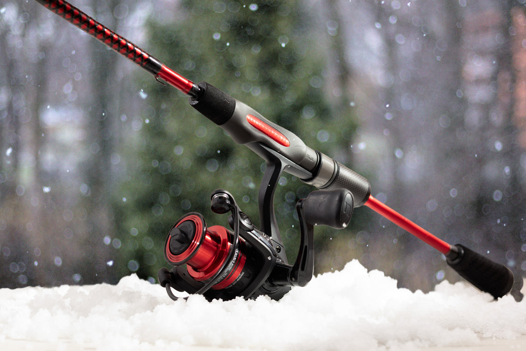Fishing rod with red and black reel on snow, blurred forest background