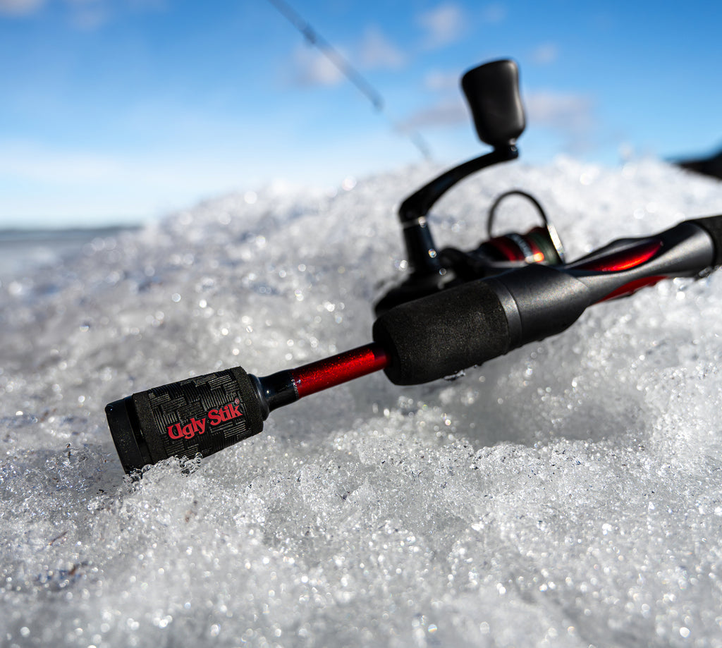 Ugly Stik Carbon Ice Spinning Rod laying flat on ice with blue skies in the background.